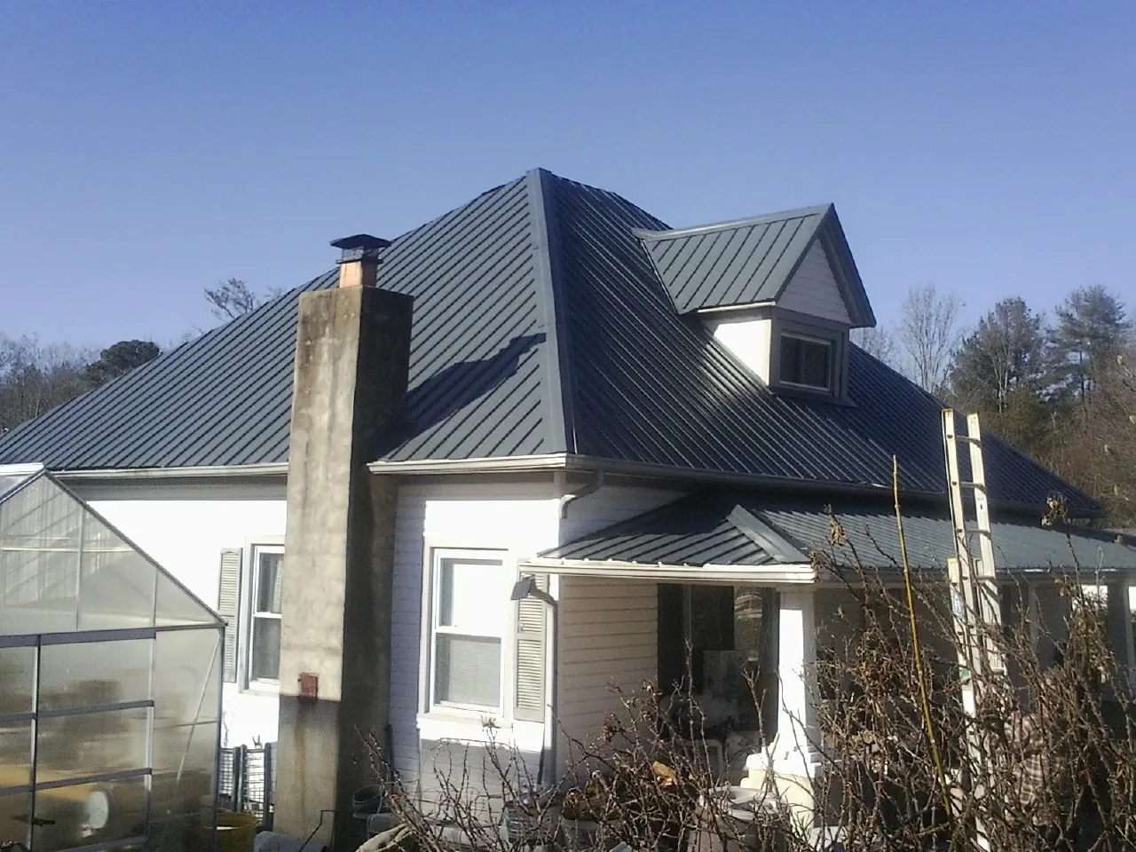 Dark blue standing seam metal roof on a white farmhouse with dormer — Slate & Tile Roof Repair by Roofing Brothers in Cressey