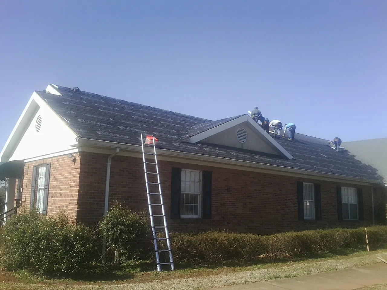 Crew tearing shingles off a brick ranch roof with a ladder set — Metal Roof Repair work by our crew in Cressey