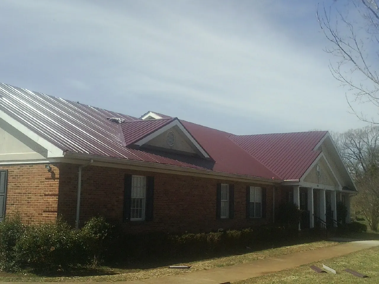 Red metal roof with gabled entries on a long brick building, from a Hail Damage Roof Repair job in Cressey