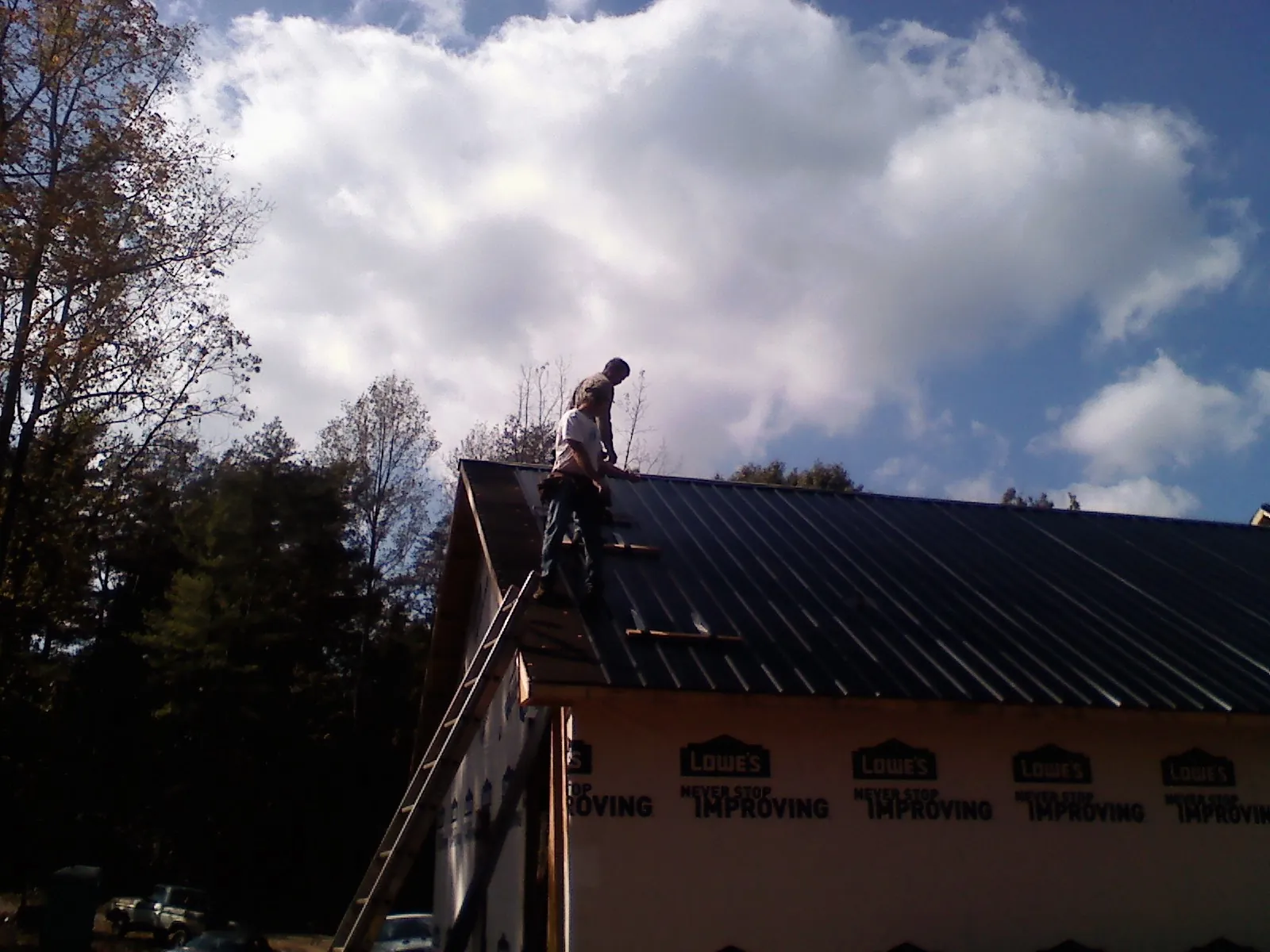 Roofer fastening dark metal panels high against a cloudy sky, from a Roof Inspection job in Cressey