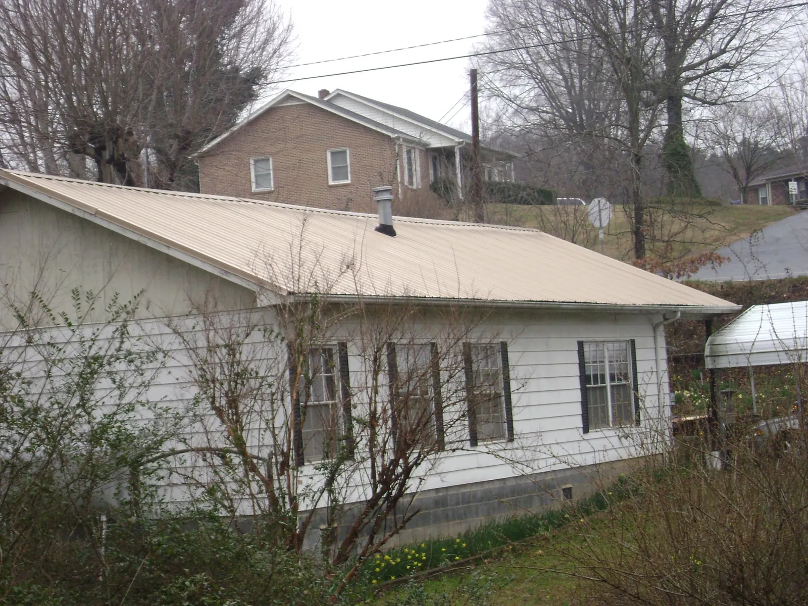 Tan metal roof on a white sided house set into a hillside — Commercial Roofing by Roofing Brothers in Cressey